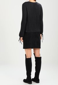 Svart ribbad tröja med lång ärm och dragsko-detaljer, kombinerad med en svart mocka mini-kjol och knähöga svarta stövlar.