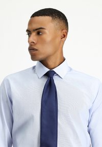 Camicia azzurro chiaro con colletto strutturato, caratterizzata da un motivo tessile. Abbinata a una cravatta blu navy unita, entrambe offrono un aspetto formale.