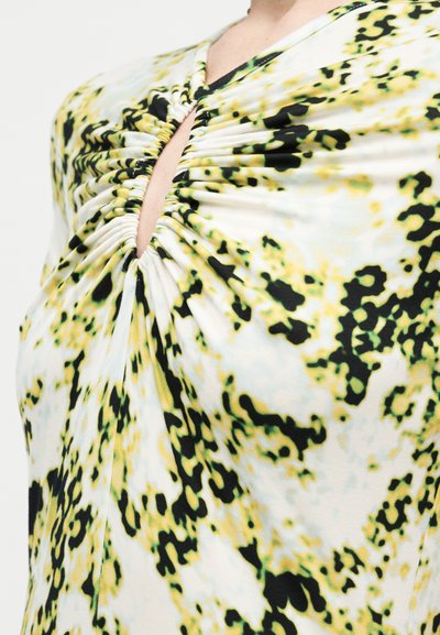 Κοντινό πλάνο ενός ατόμου που φοράει τοπ με ρυτιδωτό σχέδιο, κίτρινο, μαύρο και λευκό αφηρημένο λουλουδάτο μοτίβο και λαιμόκοψη με άνοιγμα στο κέντρο.