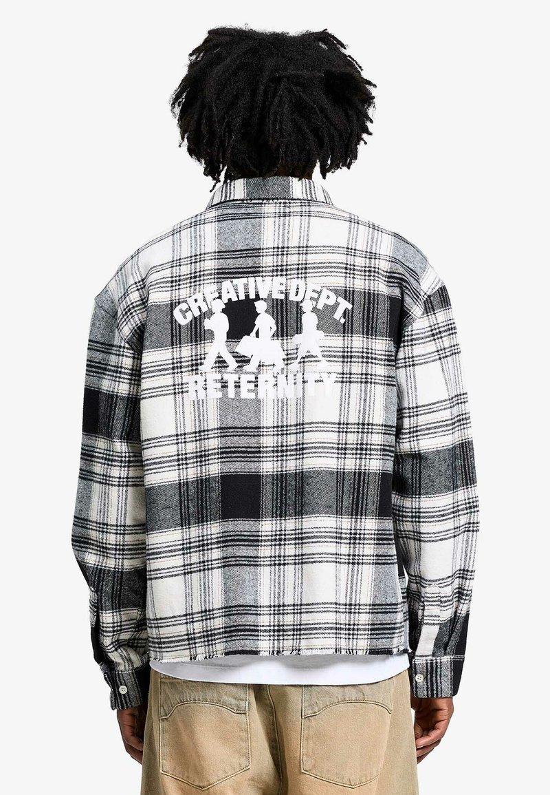 Chemise en flanelle noir et blanc avec un motif à carreaux, arborant une impression graphique disant "CREATIVE DEPT. RETENITY" dans le dos.