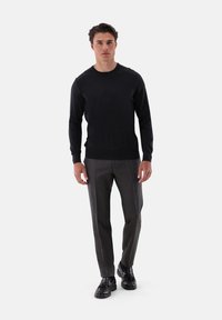 Schwarzer Langarmpullover kombiniert mit maßgeschneiderten, anthrazitgrauen Hosen und schwarzen Schuhen. Glatter Stoff mit schmaler Passform und minimaler Ausstattung.