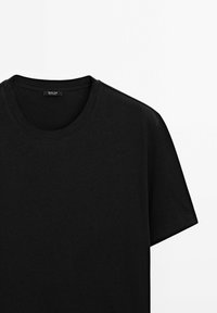 T-shirt noir uni à manches courtes et col rond avec une petite étiquette à l'intérieur du col sur fond blanc.