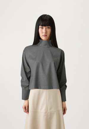 Grå, kort turtleneck med lange ermer og teksturert stoff. Båret sammen med et beige skjørt med en glatt overflate og synlige sømmer.