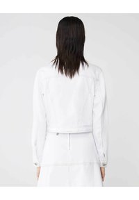 Giacca di denim bianco con maniche lunghe, design corto, tasche frontali e dettagli di cucitura visibili. Texture liscia, hardware minimale.