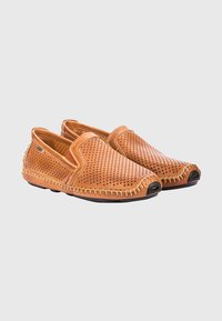 Zapatos de cuero marrón claro tipo slip-on con diseño perforado, costuras en contraste y suelas de goma; presentan punta redondeada y silueta de perfil bajo.