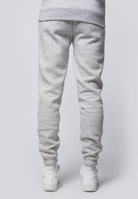 Gray sweatpants with a ribbed waistband and cuffs, made of soft material. Paired with white sneakers, featuring a flat sole and logo.
