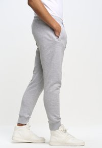 Grå sweatpants lavet af blødt materiale, med sidelommer, tapered ben og elastiske manchetter, parret med hvide høj-top sneakers.
