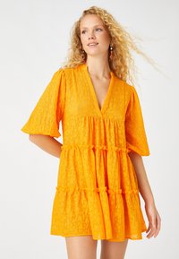 Helles oranges Kleid aus strukturiertem Stoff, mit V-Ausschnitt, kurzen weiten Ärmeln und gestuftem Design mit gerafften Details.