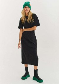 Mustast lühikeste varrukatega midikleit, sädeleva tekstuuri ja lõdva lõikega, kombineeritud mustade platvormsaabaste ja rohelise kootud mütsiga.