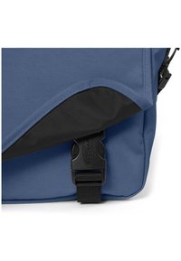 Blaues Messengertäschchen aus strukturiertem Stoff, mit einer schwarzen Klappe und verstellbarem Schnallenverschluss. Enthält ein glattes Stildetail.