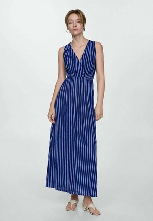 Abito maxi blu con strisce bianche verticali, design senza maniche, scollatura a V profonda, vita arricciata e tessuto morbido. Accentuato da sandali piatti.