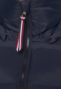 Gros plan d'une fermeture éclair de veste bleu marine avec une tirette en tissu rayé rouge, blanc et bleu attachée au curseur de la fermeture éclair.