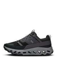 Schwarze und graue Sneaker mit einem Mesh-Obermaterial, gepolstertem Kragen, reflektierenden Akzenten und einer dicken, gepolsterten Sohle mit Ausschnitten.