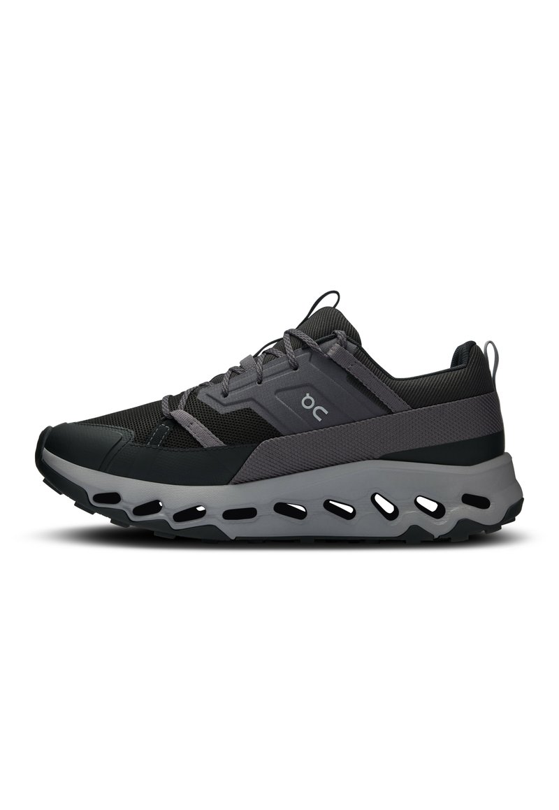 Schwarze und graue Sneaker mit einem Mesh-Obermaterial, gepolstertem Kragen, reflektierenden Akzenten und einer dicken, gepolsterten Sohle mit Ausschnitten.
