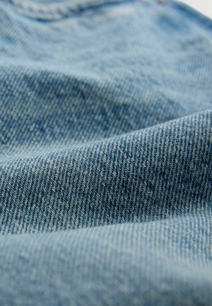 Țesătură din denim albastru deschis cu o suprafață texturată, având o țesătură clasică în diagonală și variații subtile de culoare și model.