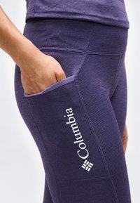 Χέρι τοποθετημένο στην πλαϊνή τσέπη μωβ ριμπ leggings με ορατό λογότυπο Columbia στον μηρό.