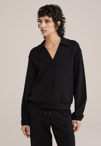 Fekete pamut pulóver mély V-kivágással és gallérral, hosszú ujjal és laza szabással, passzoló fekete nadrággal párosítva.