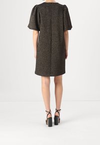 Kort svart mönstrad klänning med puffärmar, texturerad tyg och rak modell. Matchad med svarta sandaler med tjock klack.