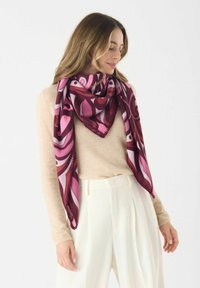 Sciarpa di seta triangolare colorata con audaci motivi rosa e bordeaux, rifinita con un punto di cucitura che crea un contrasto, indossata sopra un leggero maglione.