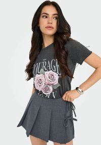 Camiseta gris con un gráfico floral que presenta rosas rosas, combinada con pantalones cortos de tela gris oscuro con pliegues atados a los lados. Textura suave, estilo casual.