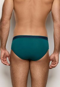 Türkise Herrenunterwäsche mit einem marineblauen Bund, der den Markennamen "yamamay" trägt. Weicher Stoff, enganliegende Passform und nahtloses Design an den Kanten.