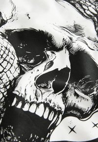 Schwarz-weiß bedruckter Stoff mit einem detaillierten Schädelmotiv, hervorgehoben durch kontrastreiche Texturen und komplexe Muster.