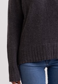 Maglione a maglia grigio scuro con orlo e polsini a coste, caratterizzato da una vestibilità ampia e una texture morbida. Indossato con jeans aderenti azzurri.