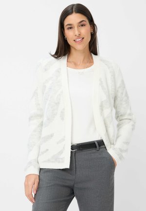 Weißer Cardigan mit weicher Textur, der ein graues abstraktes Muster aufweist, offene Vorderseite und gerippte Bündchen hat, getragen über einem weißen Oberteil und grauen Hosen.