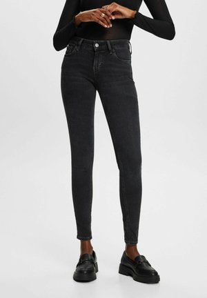 Jeans ajustados negros con cintura de altura media, cierre de botón y diseño de cinco bolsillos. La tela tiene una textura suave y ligeramente elástica.