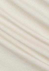 Crème-kleurige ribstof met zachte plooien en fijne verticale textuur, wat warmte en rek suggestief maakt.