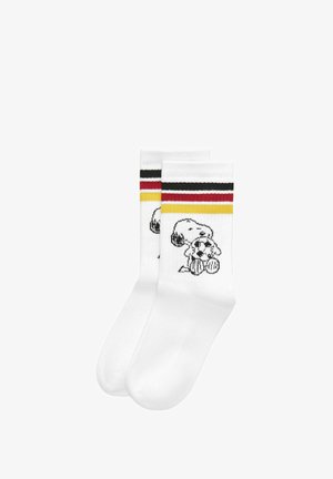 Chaussettes blanches montantes avec des rayures noires, rouges et jaunes près du haut, avec le personnage de dessin animé Snoopy tenant un ballon de football.