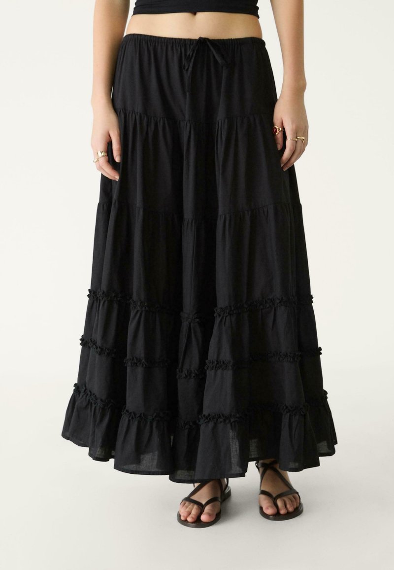 Gonna maxi nera a strati realizzata in tessuto leggero. Caratterizzata da accenti arricciati, una vita elastica con un laccetto e una silhouette morbida.