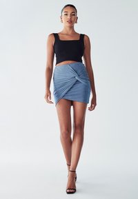 Černý bezramenný crop top se čtvercovým výstřihem, ve kterém je kombinován s světle modrou mini sukní s překládaným designem vpředu.