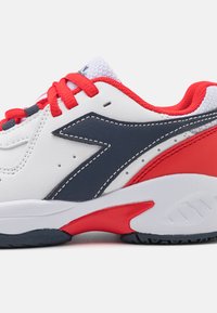 Scarpa da ginnastica bianca con accenti rossi, design laterale blu navy e linguetta in mesh testurizzato. Presenta lacci prominenti e suola imbottita.