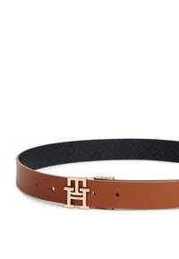 Καφέ δερμάτινη ζώνη με αγκράφα λογότυπο σε χρυσό τόνο. Το εσωτερικό έχει υφή μαύρου μοτίβου και πολλές οπές για ρύθμιση.