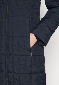 Chaqueta acolchada azul marino, con cierre de cremallera, bolsillos laterales y tejido texturizado con un patrón de rombos en la superficie.