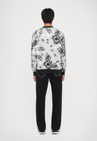 Μαύρη και γκρι φόρμα με λουλουδάτο και διακοσμητικό σχέδιο; συνδυασμένη με μαύρα κομμένα τζιν και λευκά αθλητικά υποδήματα.