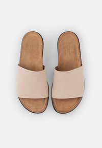 Šviesiai rudi suede šlepetės su plačiu dirželiu ir minkštu, paminkštintu vidpadžiu. Juodas guminis padas, minimalistiškas dizainas ir natūrali tekstūra.