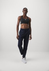 Black athletic crop top with three white stripes, paired with navy joggers featuring an elastic waistband and drawstring, and white sneakers.