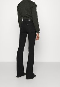 Jeans neri a zampa d'elefante con vita alta e tasca posteriore texture. Abbinati a un felpa con motivo verde scuro e strisce bianche.
