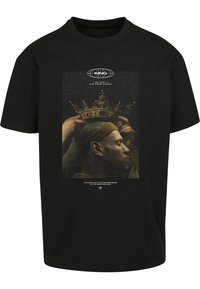 T-shirt en coton noir avec une impression graphique d'une figure couronnée portant une couronne dorée, fond texturé, et texte blanc en dessous.