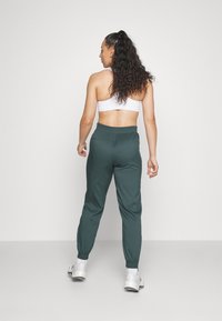 Groene joggingbroek met elastische tailleband en boorden, gecombineerd met een witte cropped top, gezien van achteren. Glad materiaal met een relaxte pasvorm.