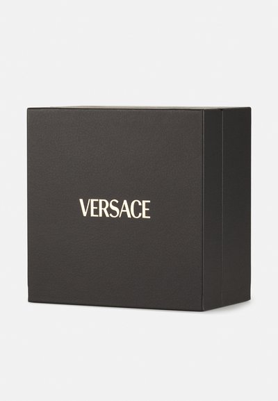 Boîte noire texturée avec une surface lisse, arborant un logo doré "VERSACE" à l'avant. Forme carrée avec des coins nets.