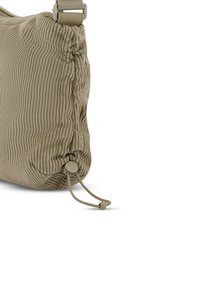Primer plano de la esquina de una bolsa de tela beige acanalada con correa ajustable y cierre con cordón fruncido en la parte inferior.