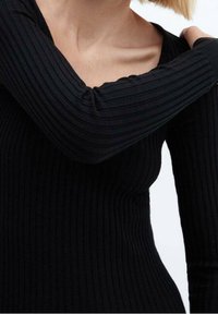 Top lungo nero a coste con maniche lunghe, caratterizzato da un scollo a V e una silhouette aderente, realizzato in un tessuto testurizzato che crea sottili linee verticali.