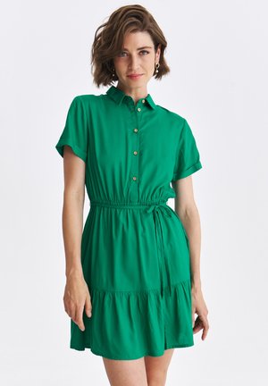 Zielona sukienka koszulowa z kołnierzykiem, krótkimi rękawami i zapięciem na guziki. Posiada elastyczny pas oraz falbaniasty dół. Wykonana z miękkiego materiału.