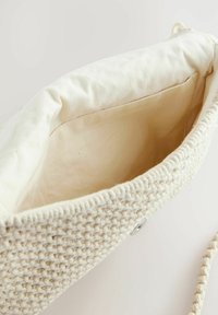 Gewebte beige Tasche mit einem weichen, cremefarbenen Innenraum. Sie verfügt über ein strukturiertes Äußeres, einen magnetischen Druckverschluss und einen geflochtenen Tragegurt.