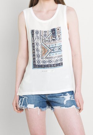 Haut sans manches blanc avec un motif graphique présentant des designs géométriques en bleu, marron et blanc, associé à un short en denim déchiré.