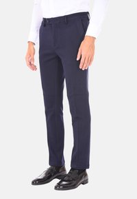 Pantaloni blu scuro con una vestibilità sartoriale, realizzati in un tessuto liscio. Presentano una chiusura con bottone e tasche laterali, abbinati a mocassini neri.