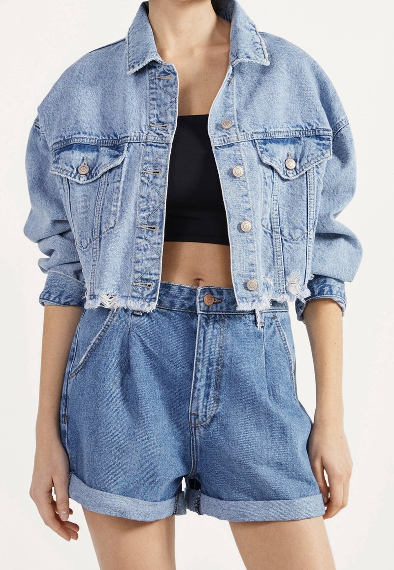 Ensemble en denim composé d'une veste et d'un short ; couleur bleu clair ; design court avec des bords effilochés, des fermetures à boutons et deux poches poitrine. Texture lisse.